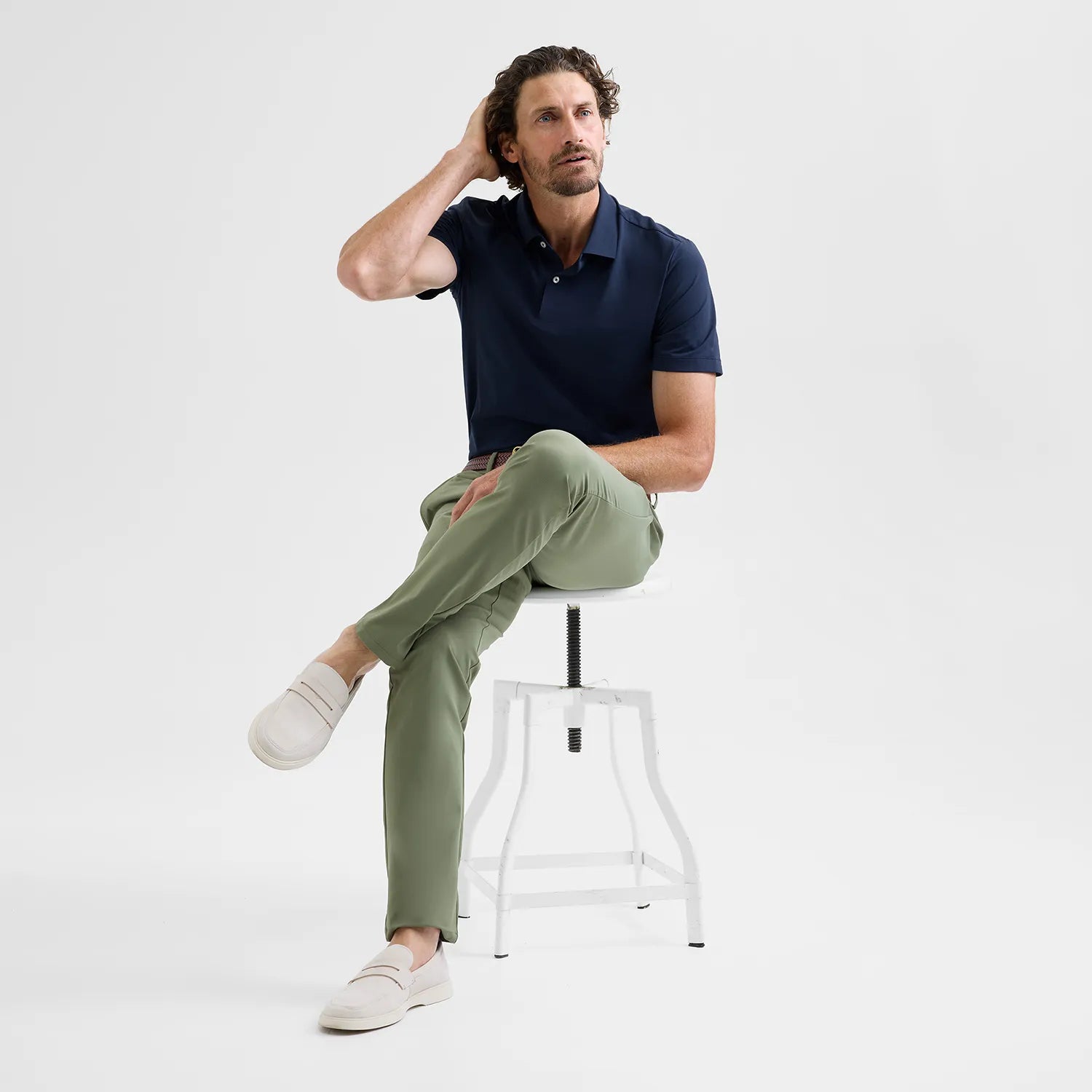 Model sitting on a stool wearing Olive Positano Travel Chino, showcasing Polygiene StayFresh® technology that resists odors, perfect for extended wear and light packing.