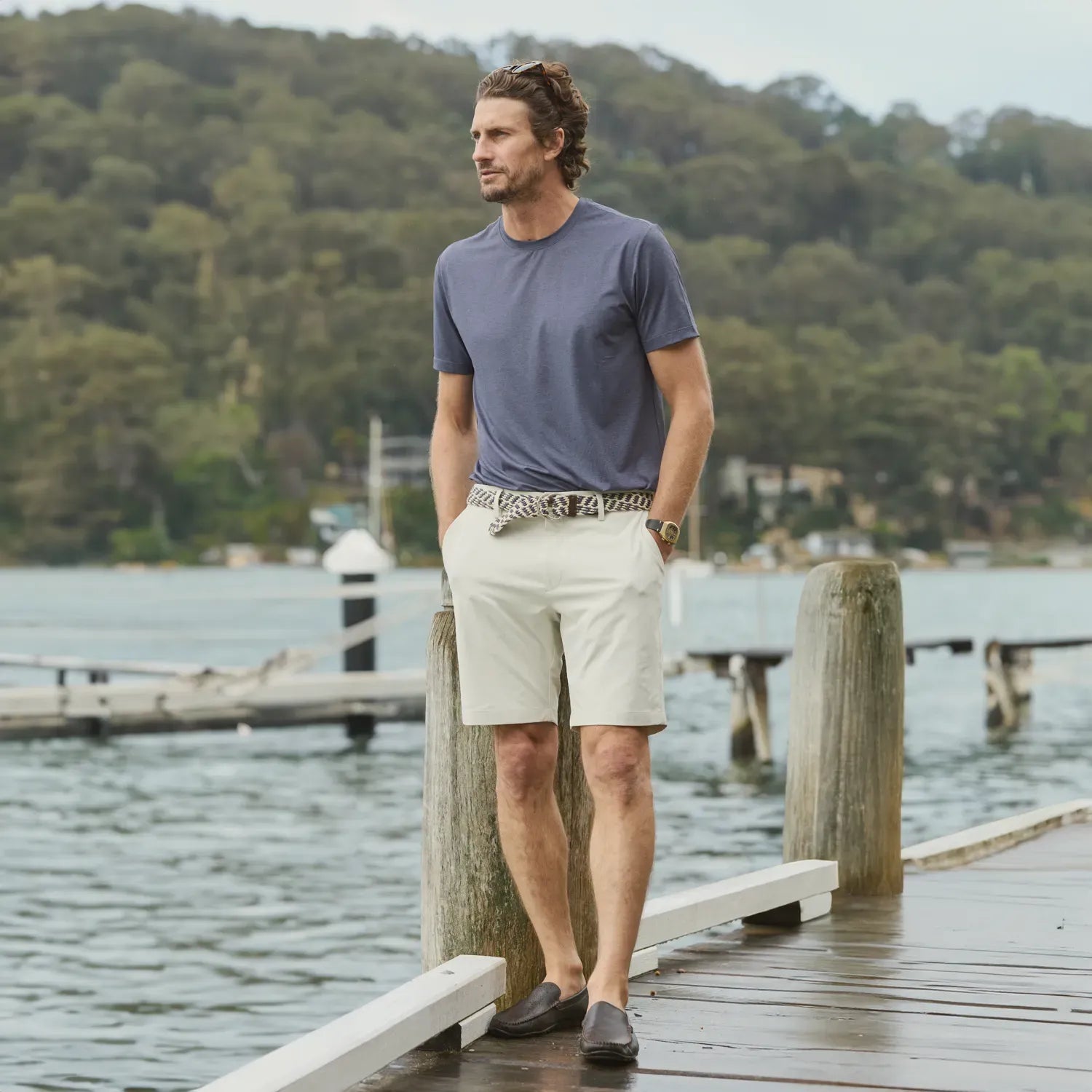 Man standing on a wooden dock by a body of water with trees in the background